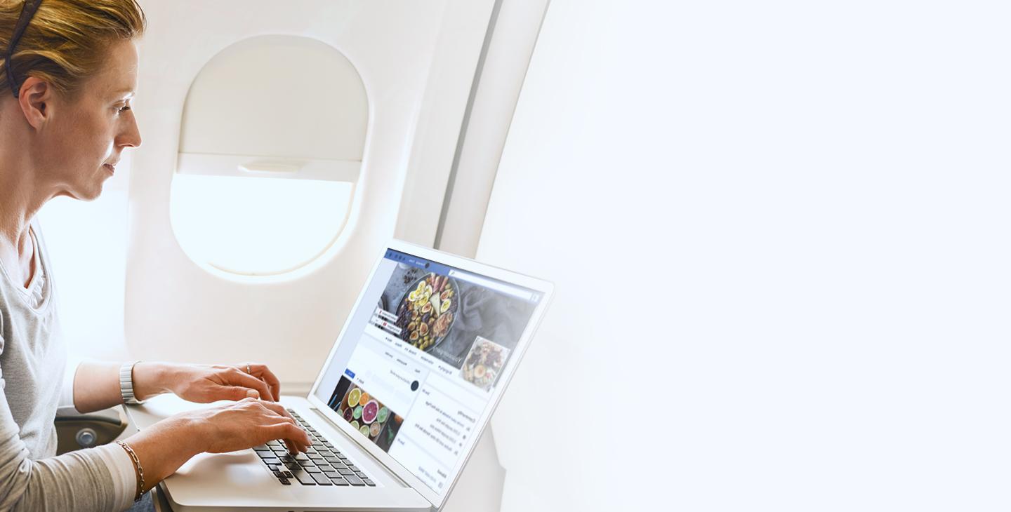 Woman sitting on a plane using inflight connectivity to browser Facebook on her laptop